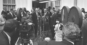 Lyndon Johnson standing in front of a bank of microphones giving a press conference