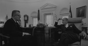 Larry O'Brien and LBJ sit around a desk in the Oval Office