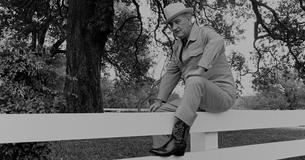 LBJ wearing cowboy boots, sitting on a fence 