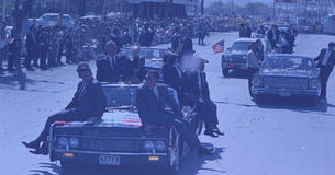 LBJ in a car, waving to a crowd, surrounded by Secret Service officers