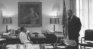 Robert McNamara sitting and talking to LBJ standing